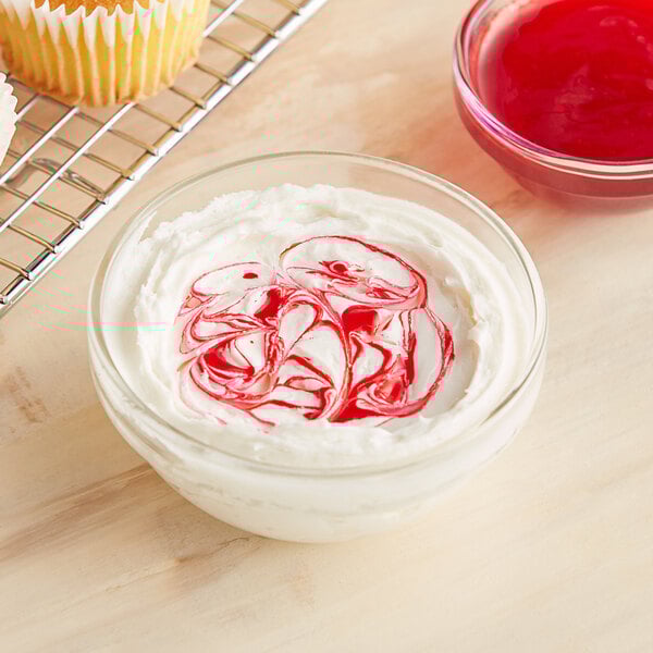 A bowl of white frosting with red swirls on top of a cupcake.