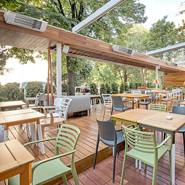 An Aura carbon stainless steel infrared patio heater on a wooden deck with tables and chairs.