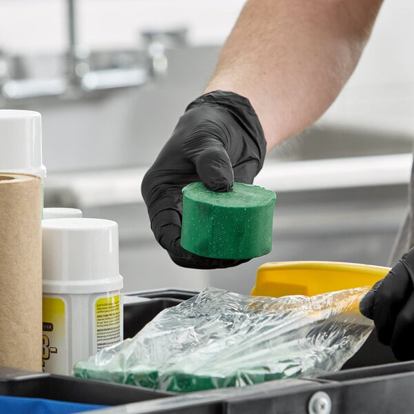 A green enzymatic concentrated grease trap block being held by a person wearing black gloves.