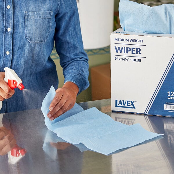 A woman using a blue Lavex industrial wiper to clean a table.