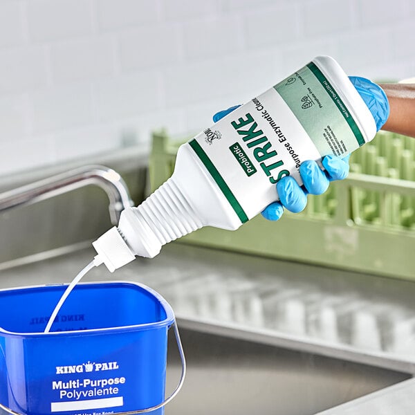 A gloved hand pours Noble Eco Strike Enzymatic Cleaner into a blue bucket.