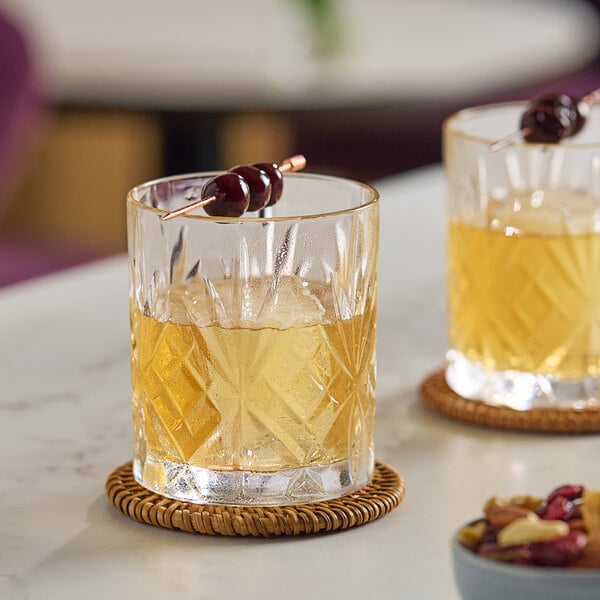 Two Schott Zwiesel double old fashioned glasses of yellow liquid with cherries on a stick.