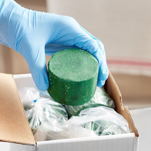 A hand in blue gloves holding a green Noble Eco Enzo-Kleen grease trap block.