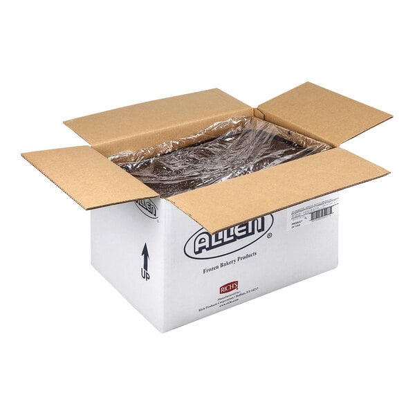 An open cardboard box containing a large, rectangular, plastic-wrapped chocolate cake.
