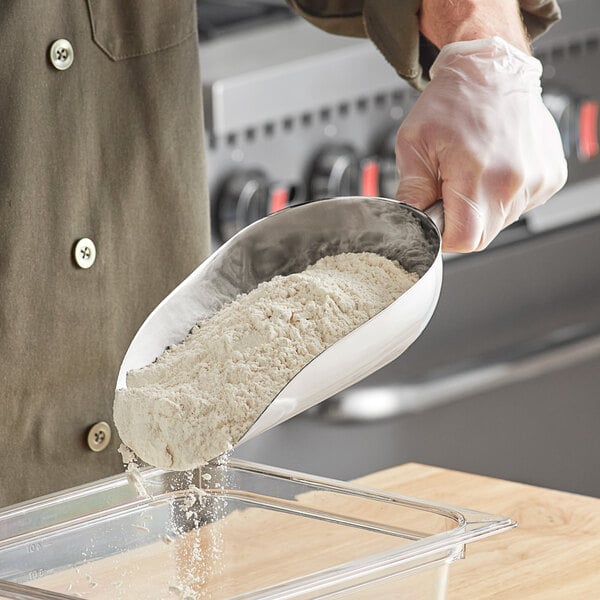 A person using a Choice stainless steel scoop to pour flour into a container.