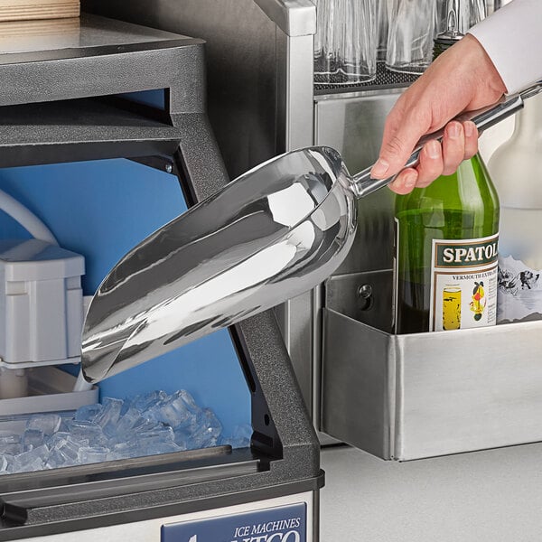 A hand using a Choice stainless steel scoop to scoop ice into a glass.
