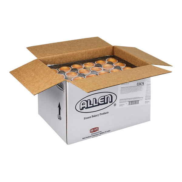 An open cardboard box containing multiple rows of un-iced yellow cupcakes in paper liners.