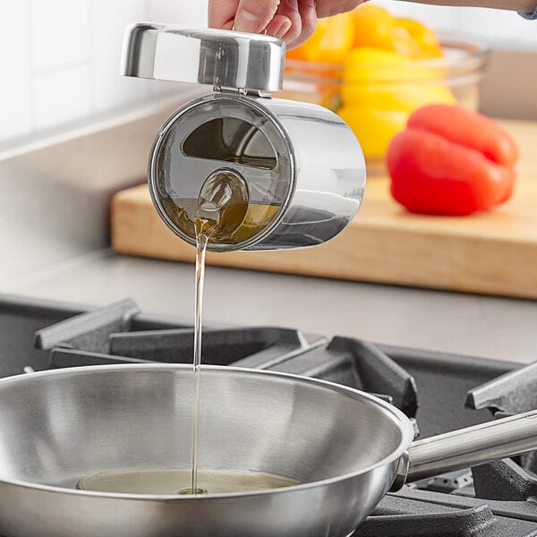 A person using a Choice stainless steel oil container to pour oil into a frying pan.