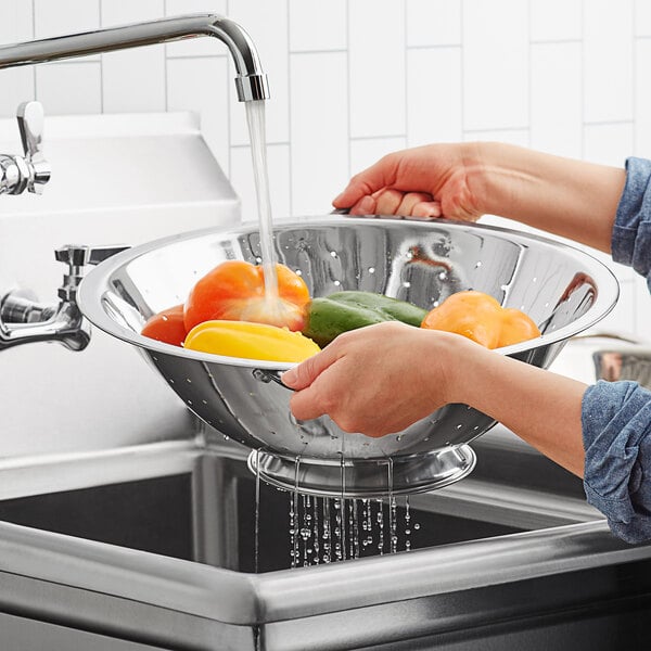 A person pouring water from a bowl of peppers into a Choice stainless steel colander.