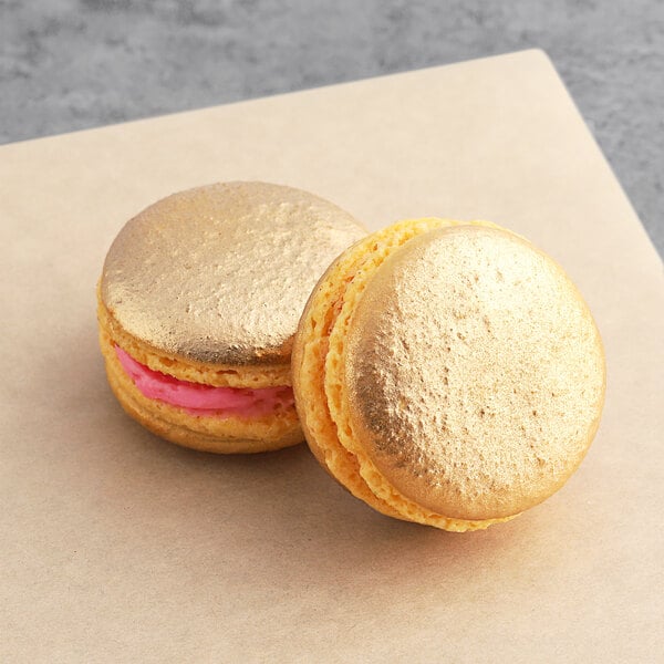 Two gold Macaron Centrale raspberry macarons on a table.