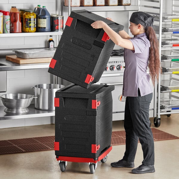 A woman using a compact dolly to carry a large black CaterGator Dash pan carrier box.