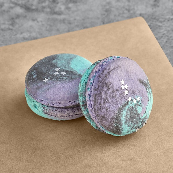 Two Macaron Centrale Galaxy macarons with purple and blue stars on them.