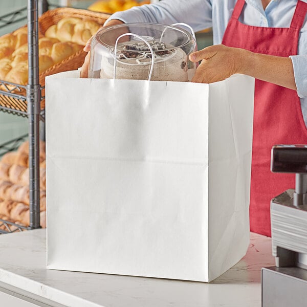 A woman holding a white Duro paper shopping bag with handles full of food.