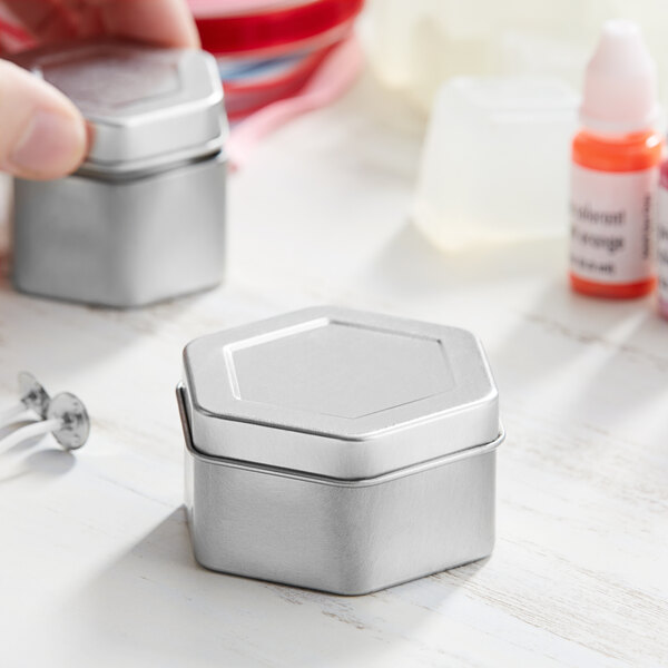 A hand holding a silver hexagon-shaped metal tin with a slip cover.