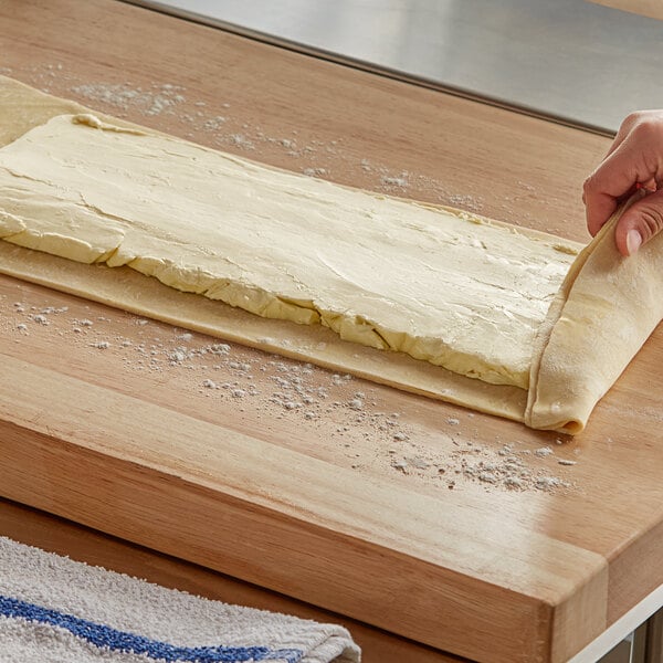 A person rolling out dough with Melt Organic Unsalted Butter on a wooden surface.