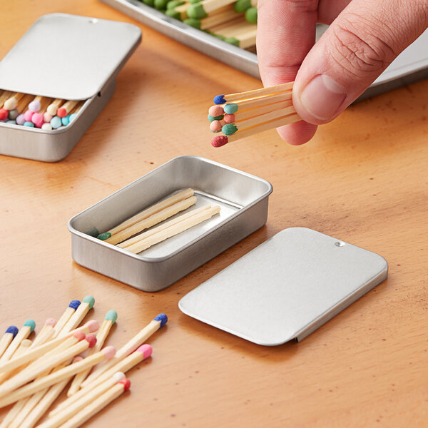 A hand holding matches in a silver medium tin with a slide top.