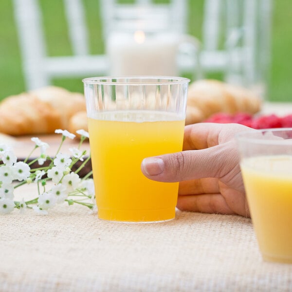 A clear plastic fluted tumbler filled with orange juice on a table.