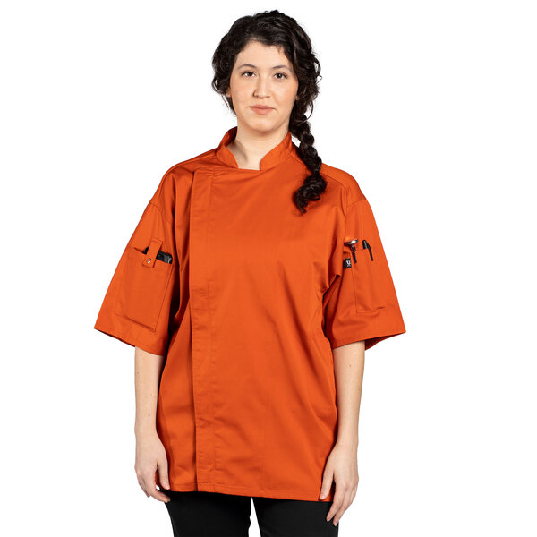 An orange Uncommon Chef Venture Pro chef coat with black buttons on a woman.