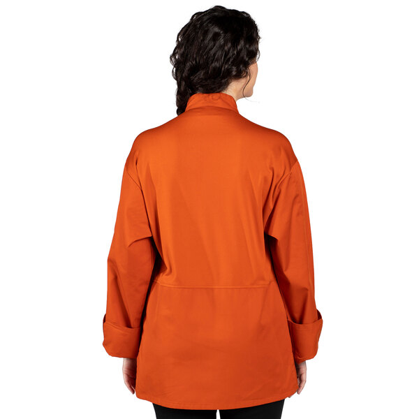 A woman wearing an orange Uncommon Chef Endeavor Pro Vent long sleeve chef coat with mesh on the back.
