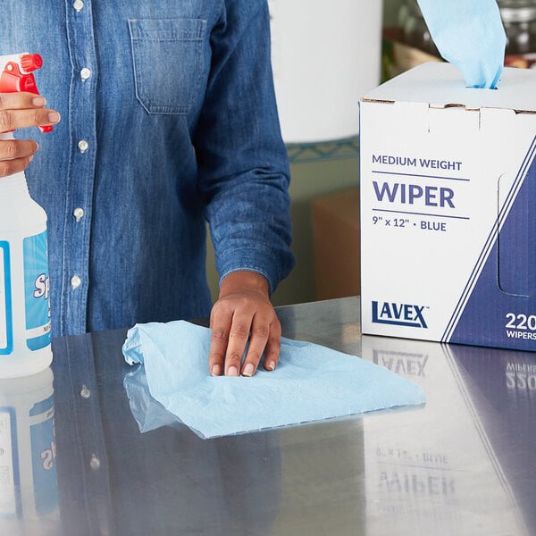 A woman cleaning a counter with a Lavex blue industrial wiper.