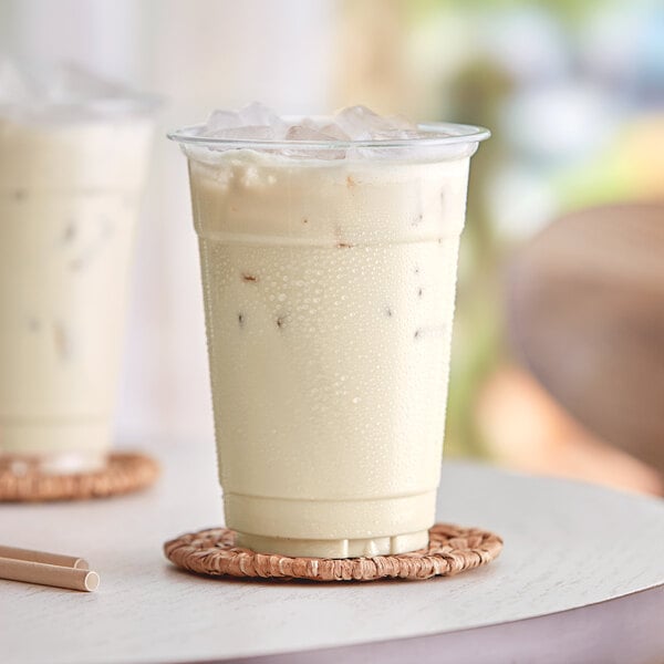 A glass of white Capora White Chocolate Frappe with a straw.