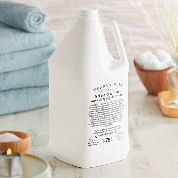 A white plastic bottle of Pharmacopia Verbena conditioner on a table next to towels.