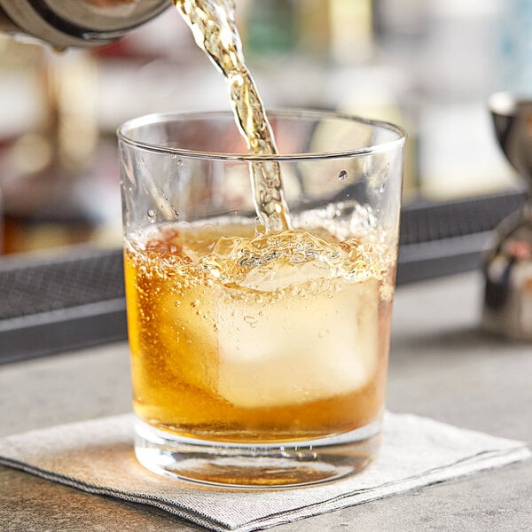 A hand pouring whiskey into an Acopa Straight Up Rocks Glass filled with ice.