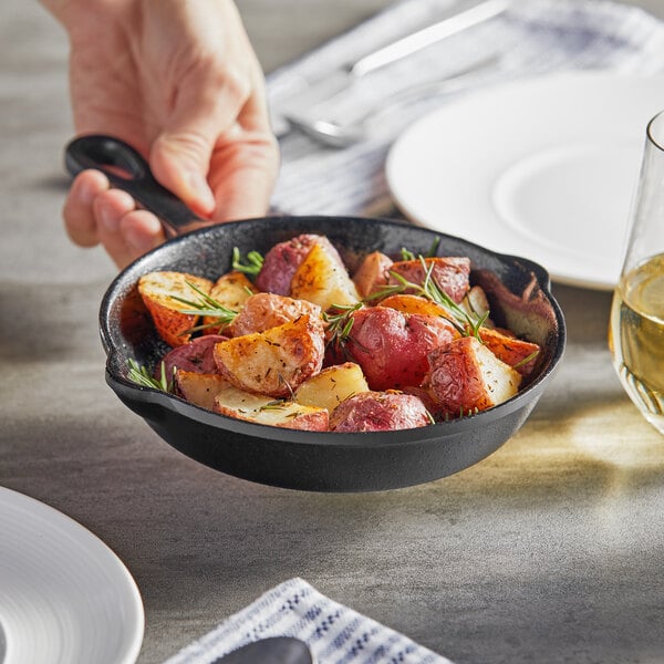 A hand holding an Acopa faux cast iron skillet filled with rosemary potatoes.