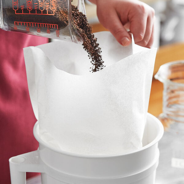 A hand holding a Toddy paper filter over a measuring cup of coffee.