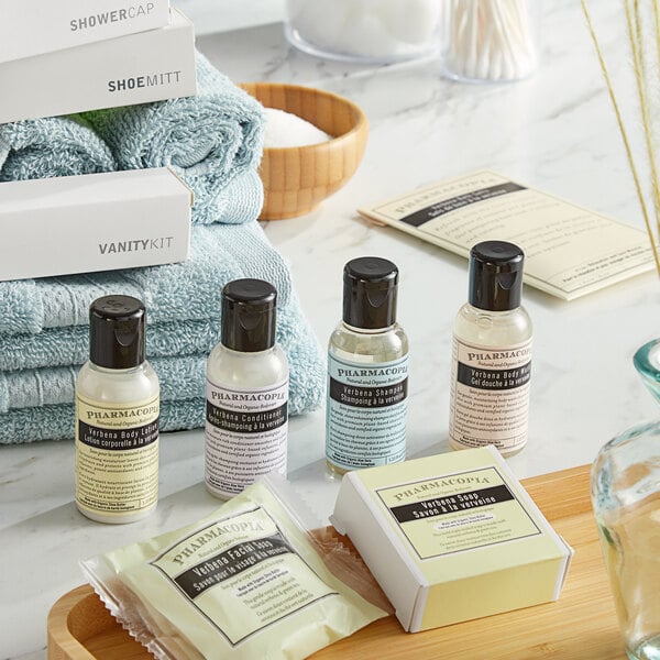 A case of Pharmacopia Verbena body soap bottles on a table with blue towels.