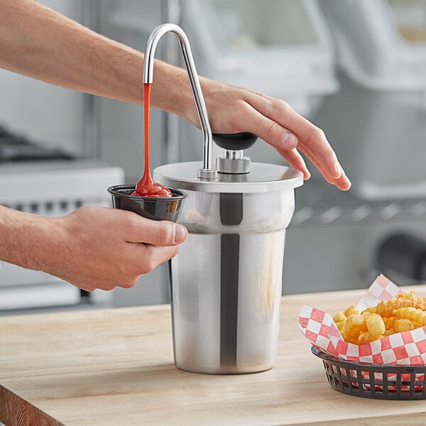 A close-up of a hand using a ServSense stainless steel pump to pour ketchup into a silver cup.