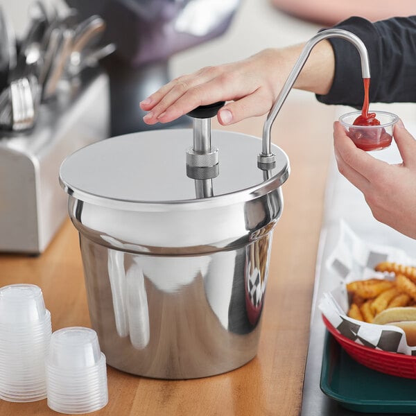 A person using a ServSense stainless steel pump to dispense sauce into a plastic cup.