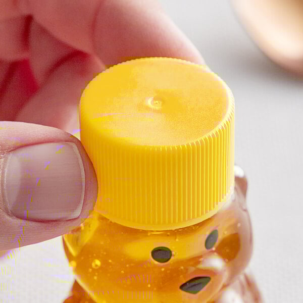 A person holding a small plastic bottle of honey with a yellow 24/410 ribbed cap.