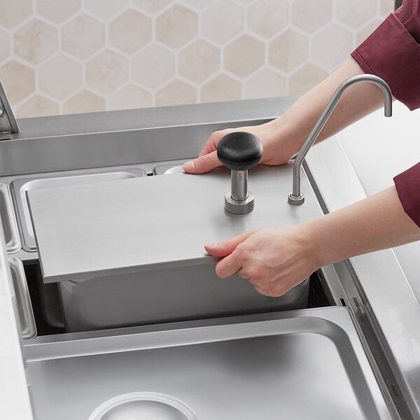 A person using a ServSense stainless steel pump dispenser to fill a metal container.