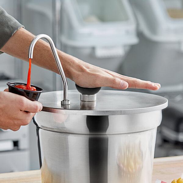 A person using a ServSense stainless steel pump to pour red sauce into a bowl.