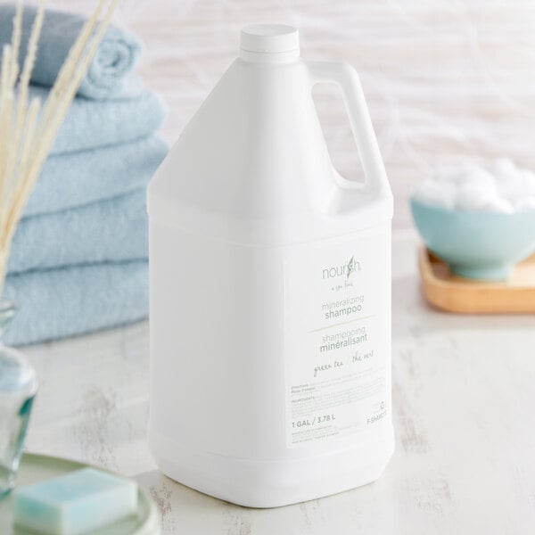 A case of white Nourish Green Tea Shampoo bottles on a table next to blue towels.