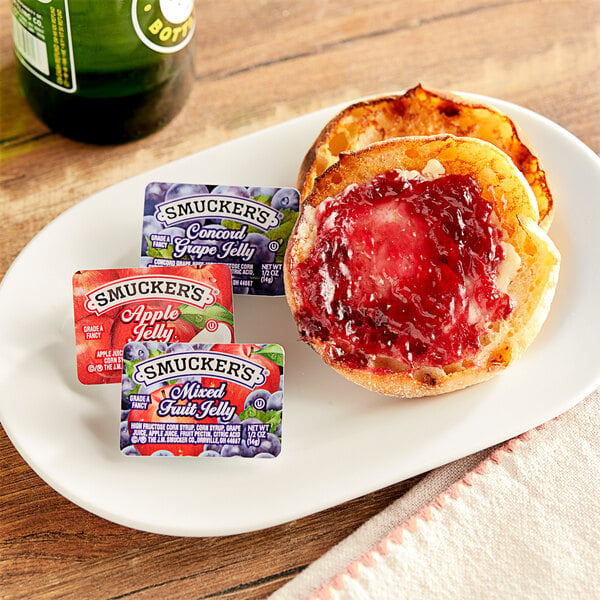 A plate with a jam and jelly sandwich and Smucker's portion cups on a table.