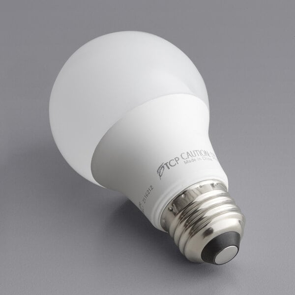 A TCP Pro Line frosted LED light bulb on a gray surface.