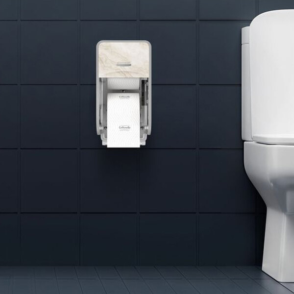 A wall-mounted vertical toilet paper dispenser with a marble-like cover is installed next to a white toilet against dark tiled walls.