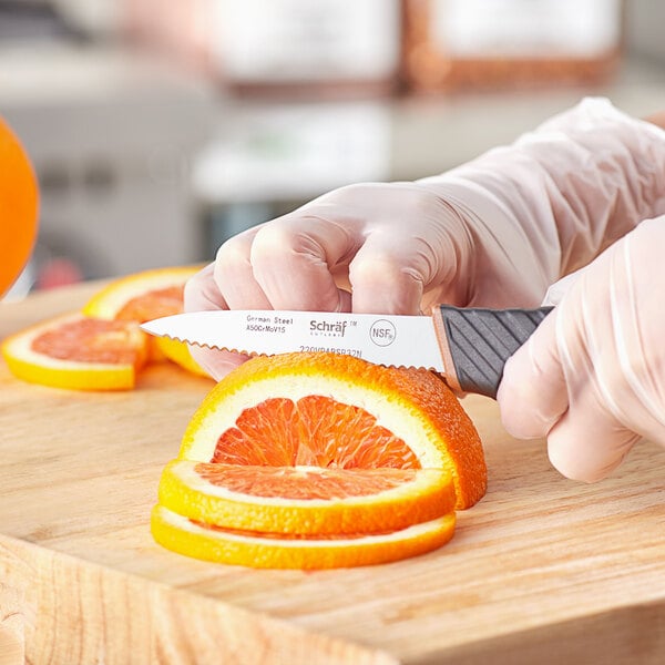 A hand using a Schraf serrated paring knife to slice an orange.