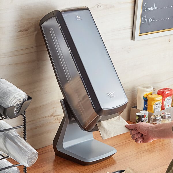 A hand holding a black Dixie Ultra napkin tower on a countertop.