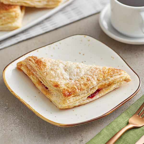 A plate with a sugared cherry turnover and a fork on it next to a cup of coffee.