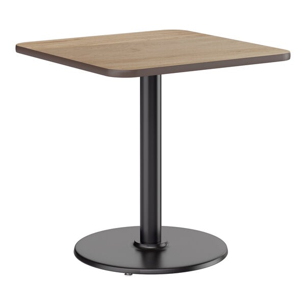 A square standard height table with a reversible white birch or ash laminated top and a black cast iron pedestal base.