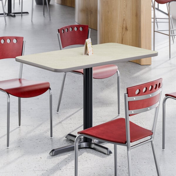 A rectangular reversible gray and white laminated table with a black cast iron base, surrounded by red and chrome chairs in a dining area.