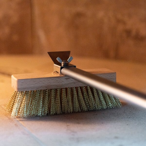 A brush with brass bristles, a wooden block, a metal handle, and a metal scraper attached to the top.