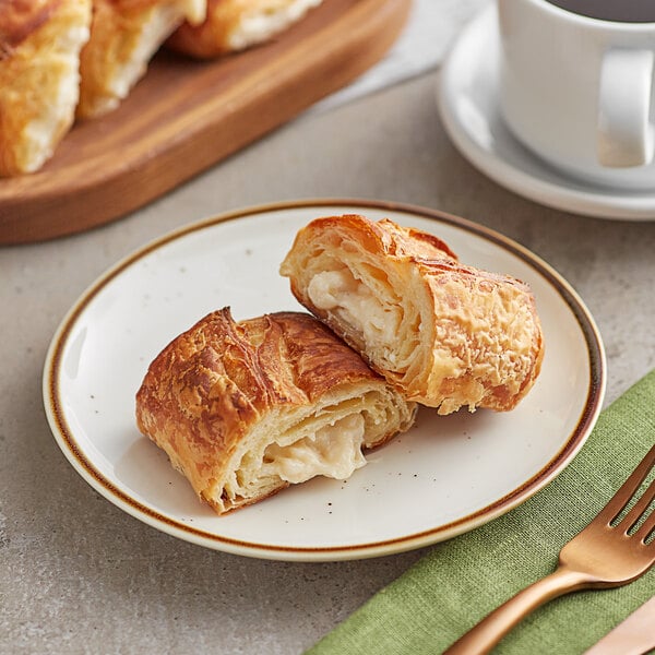 A plate with two Orange Bakery ready to bake cream cheese filled croissants and a cup of coffee.