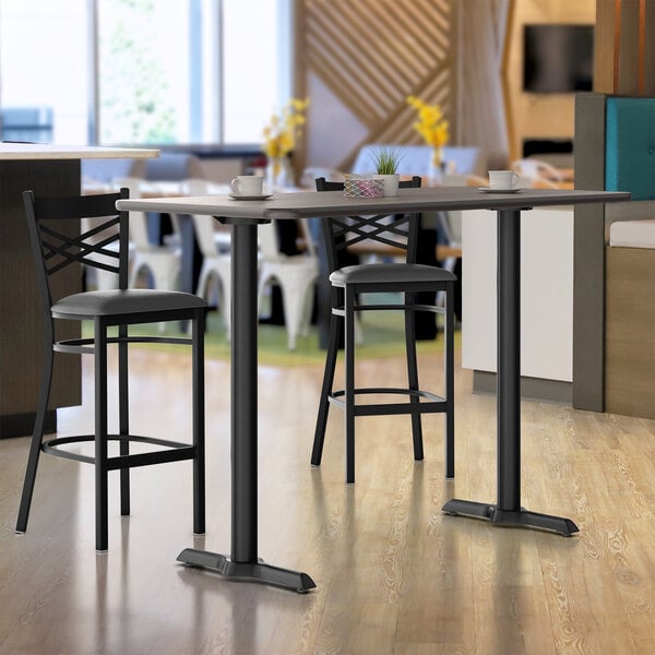 A Lancaster Table & Seating bar table with a white birch and ash top on a black pole base.