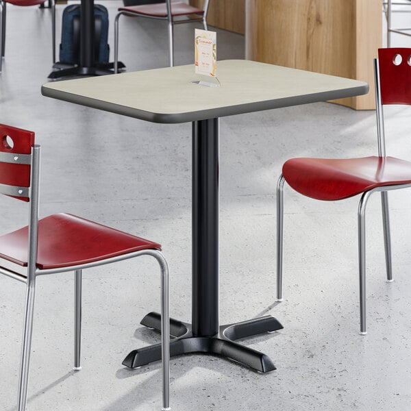 A rectangular reversible gray and white laminated table with a black cast iron base, shown with red chairs in a dining area.