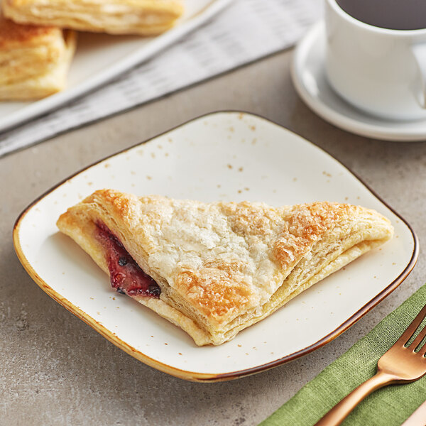 A plate with a sugared blueberry turnover next to a cup of coffee.