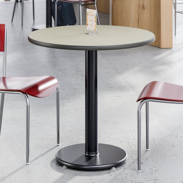 A round, standard height table with a reversible gray and white laminated top and a black cast iron base.